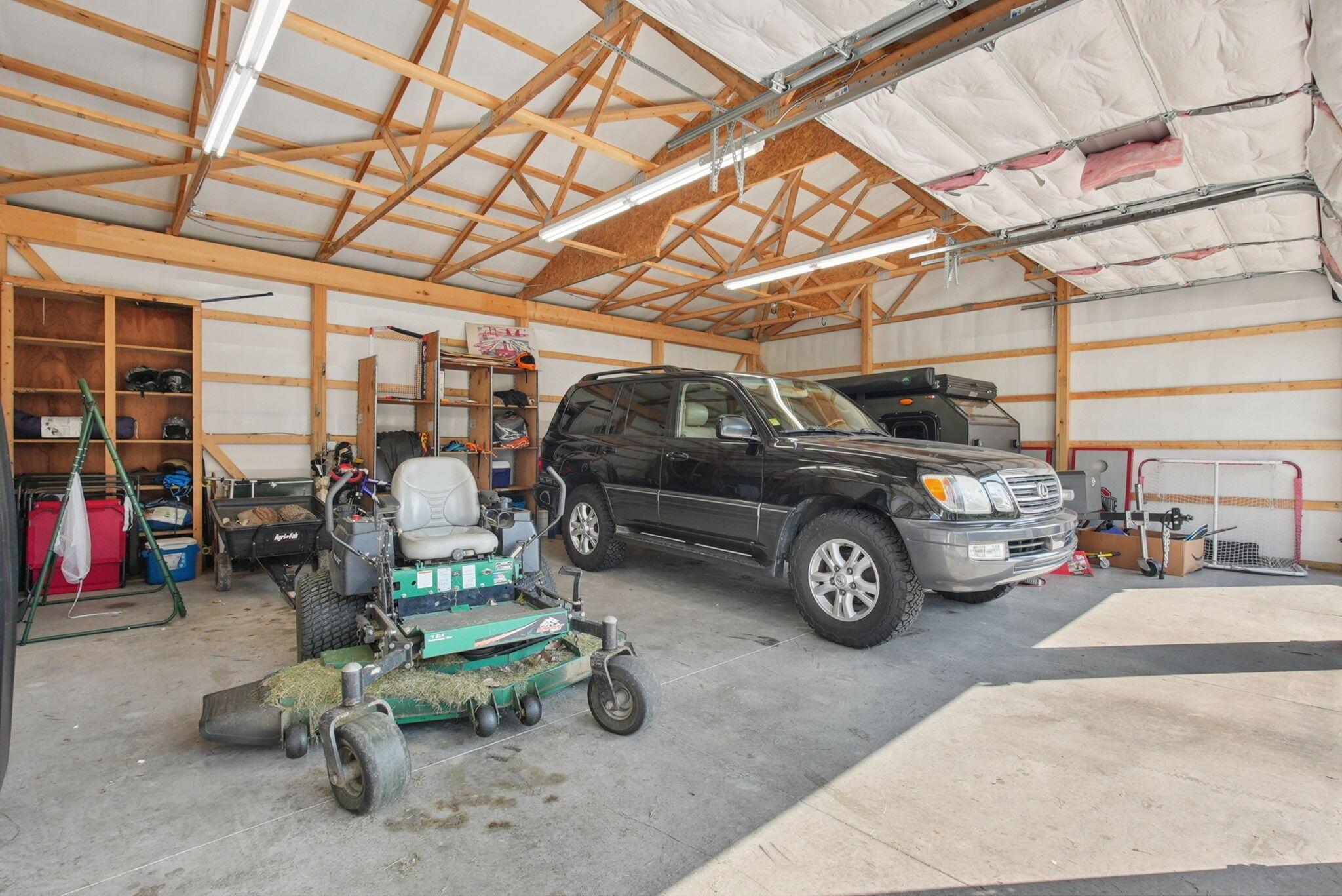 9435 Concord Road Powell, OH 43065 - Photo 48 of 77 Spacious garage with exposed wood beam ceiling, multiple fluorescent light fixtures, built-in shelving, and a concrete floor