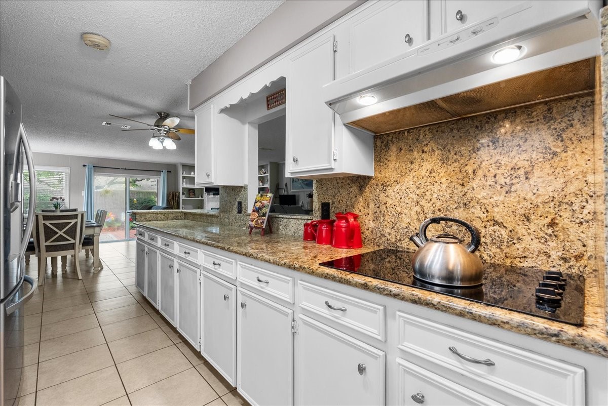 883 Silverpines Road Houston, TX 77062 - Photo 12 of 38 This photo showcases a bright, spacious kitchen with white cabinetry and granite countertops. It features a sleek stovetop, stainless steel appliances, and ample storage, leading to a dining area with large windows and a view of the backyard.