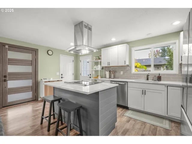 a kitchen with stainless steel appliances a sink a stove a refrigerator cabinets and wooden floor