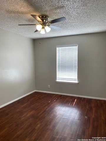 an empty room with wooden floor chandelier fan and windows