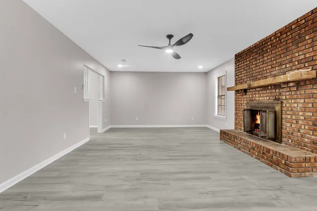 a view of an empty room with wooden floor fireplace and a window
