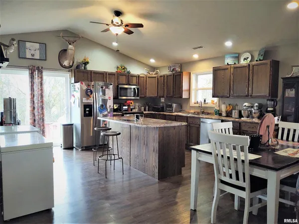 a kitchen with stainless steel appliances kitchen island granite countertop a table chairs and a refrigerator