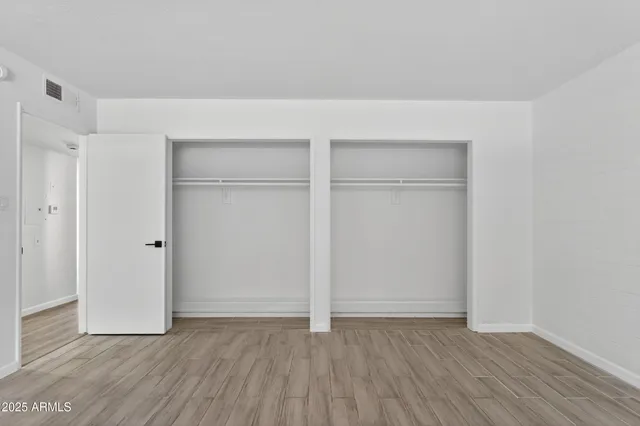a view of an empty room with wooden floor and closet