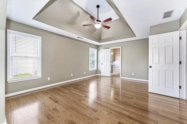an empty room with wooden floor fan and windows