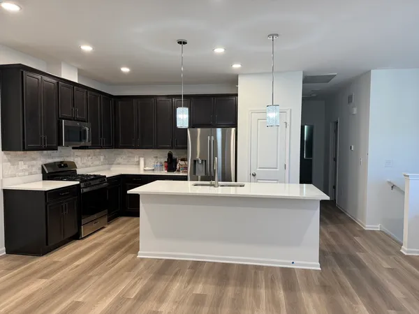 a large white kitchen with kitchen island a refrigerator a stove a sink and a oven with wooden floor