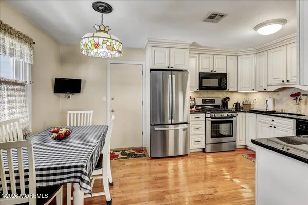 a kitchen with stainless steel appliances kitchen island granite countertop a refrigerator a stove a sink dishwasher a dining table and chairs with wooden floor