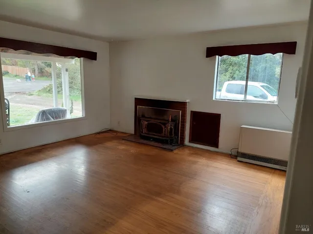 an empty room with wooden floor fireplace and windows