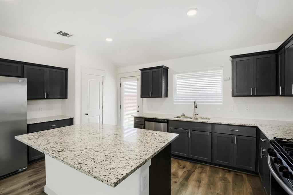1368 Cedar Street Forney, TX 75126 - Photo 11 of 29 Kitchen featuring dark shaker-style cabinetry, light speckled countertops, stainless steel appliances, a center island, and wood-finish flooring