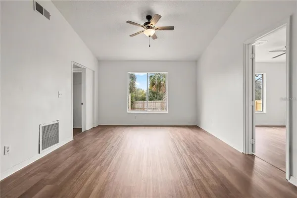 an empty room with wooden floor chandelier fan and windows