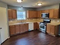 a kitchen with stainless steel appliances granite countertop wooden cabinets a sink a stove a refrigerator and microwave with wooden floor
