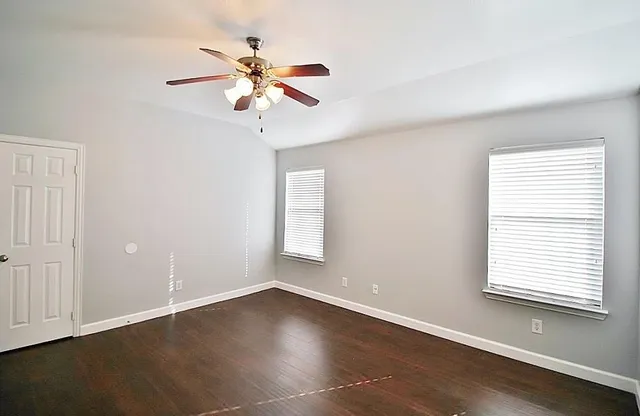 an empty room with wooden floor fan and windows