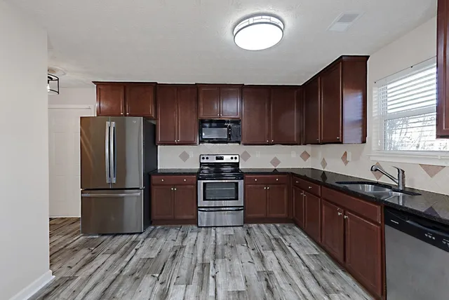 a kitchen with granite countertop wooden floors stainless steel appliances and a window