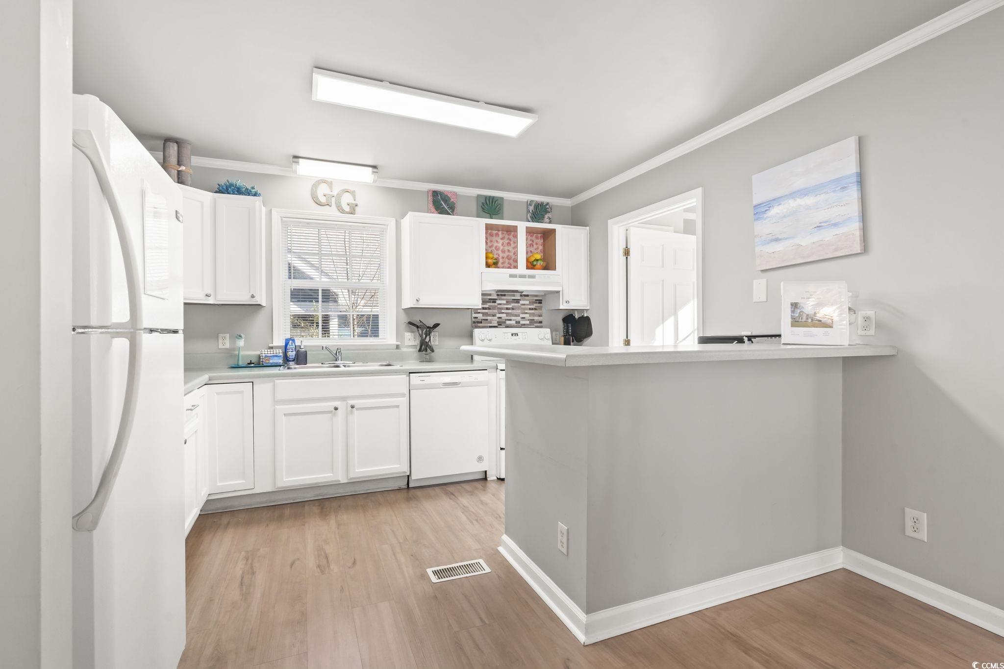 409 Knoll Court Myrtle Beach, SC 29588 - Photo 8 of 33 Kitchen featuring white appliances, light countertops, white cabinets, crown molding, and under cabinet range hood