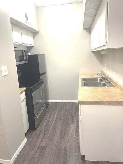 3316 Guadalupe Street, Unit 209 Austin, TX 78705 - Photo 6 of 12 Kitchen with white cabinetry, light countertops, dark wood-style flooring, and black range with electric cooktop