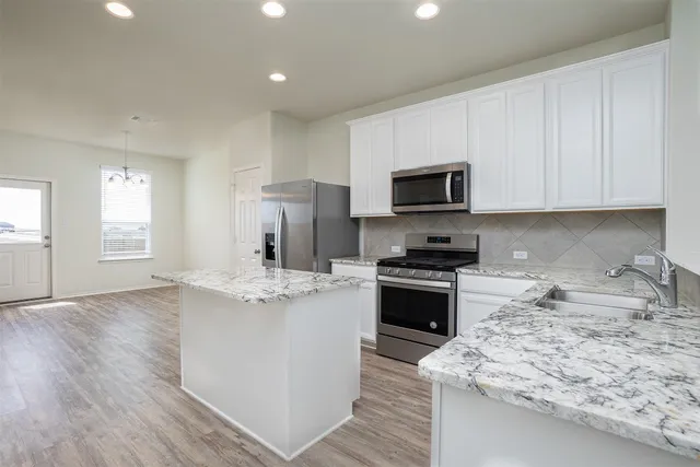 a kitchen with kitchen island granite countertop a stove top oven a sink dishwasher and a refrigerator with wooden floor