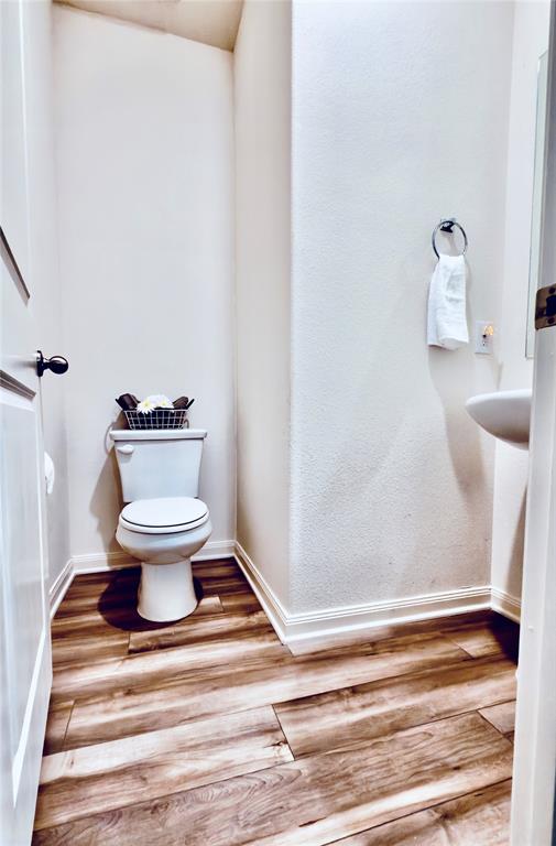 196 Cattlemans Crk Road West Newark, TX 76071 - Photo 15 of 31 Powder room featuring wood-finish flooring, a white commode, and a pedestal sink with a wall-mounted faucet