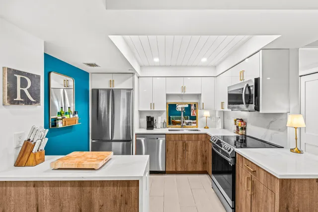 a kitchen with stainless steel appliances kitchen island granite countertop a refrigerator a stove top oven a sink dishwasher and white cabinets with wooden floor