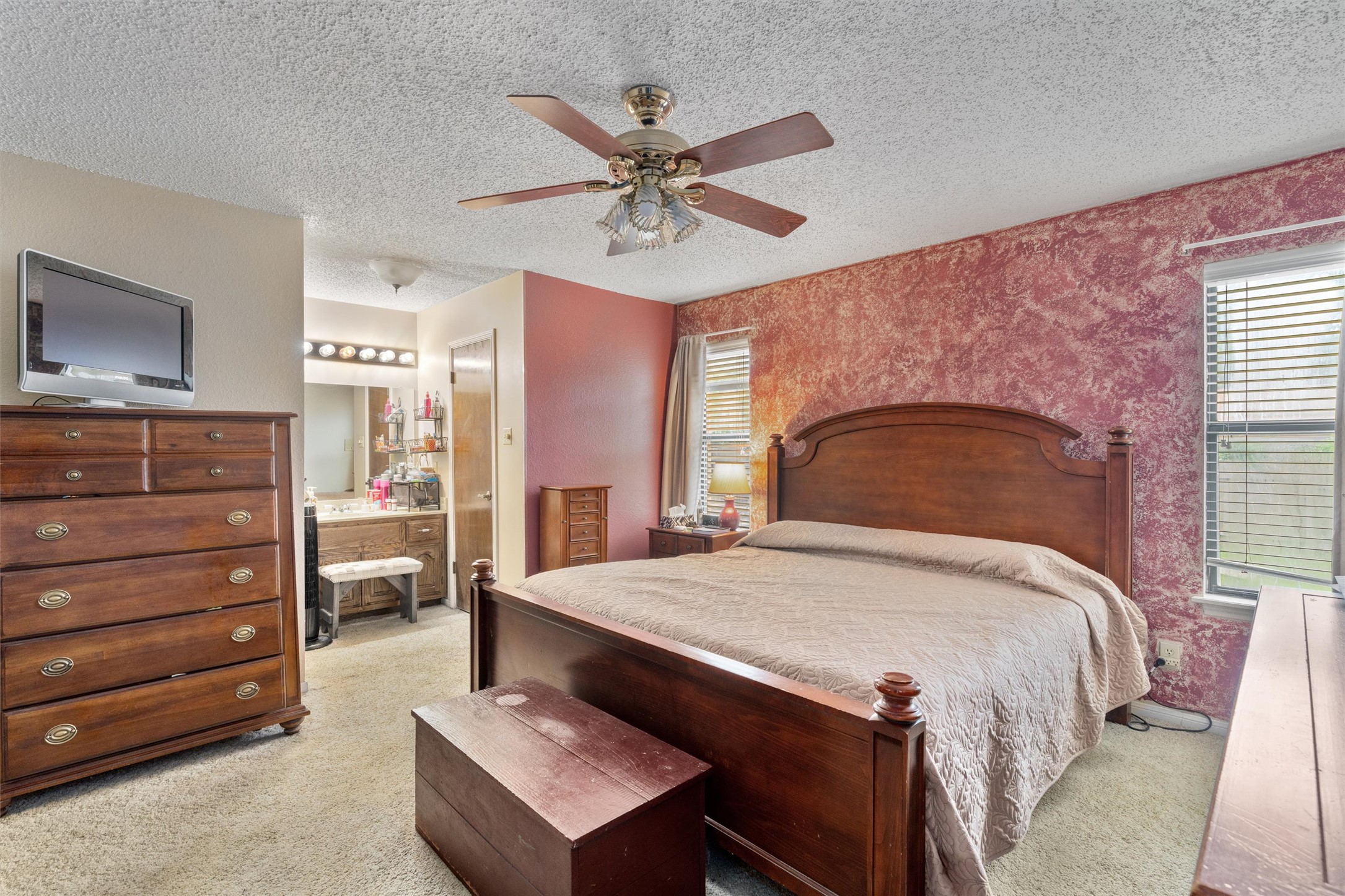 401 Drake Lane Taylor, TX 76574 - Photo 14 of 31 Carpeted bedroom featuring a ceiling fan, two windows with blinds, and an attached vanity area with a mirror and multi-bulb light fixture