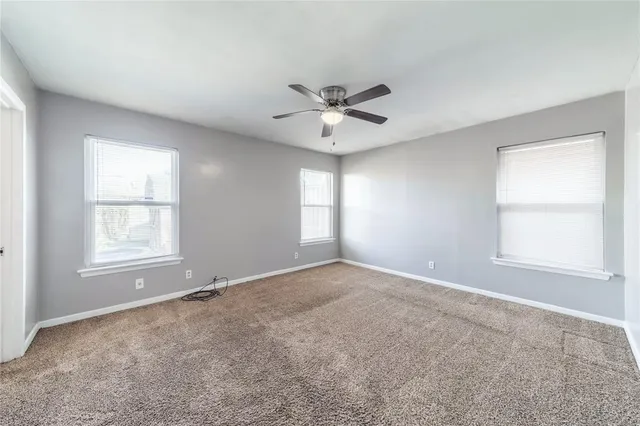 an empty room with chandelier fan and windows