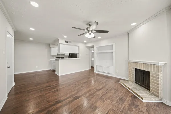 an empty room with wooden floor a ceiling fan a fireplace and windows