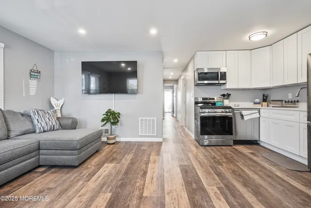 a living room with stainless steel appliances furniture cabinets and a wooden floor
