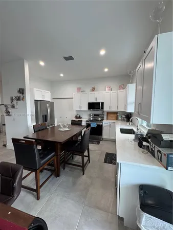 a living room with stainless steel appliances kitchen island granite countertop a table chairs and a refrigerator