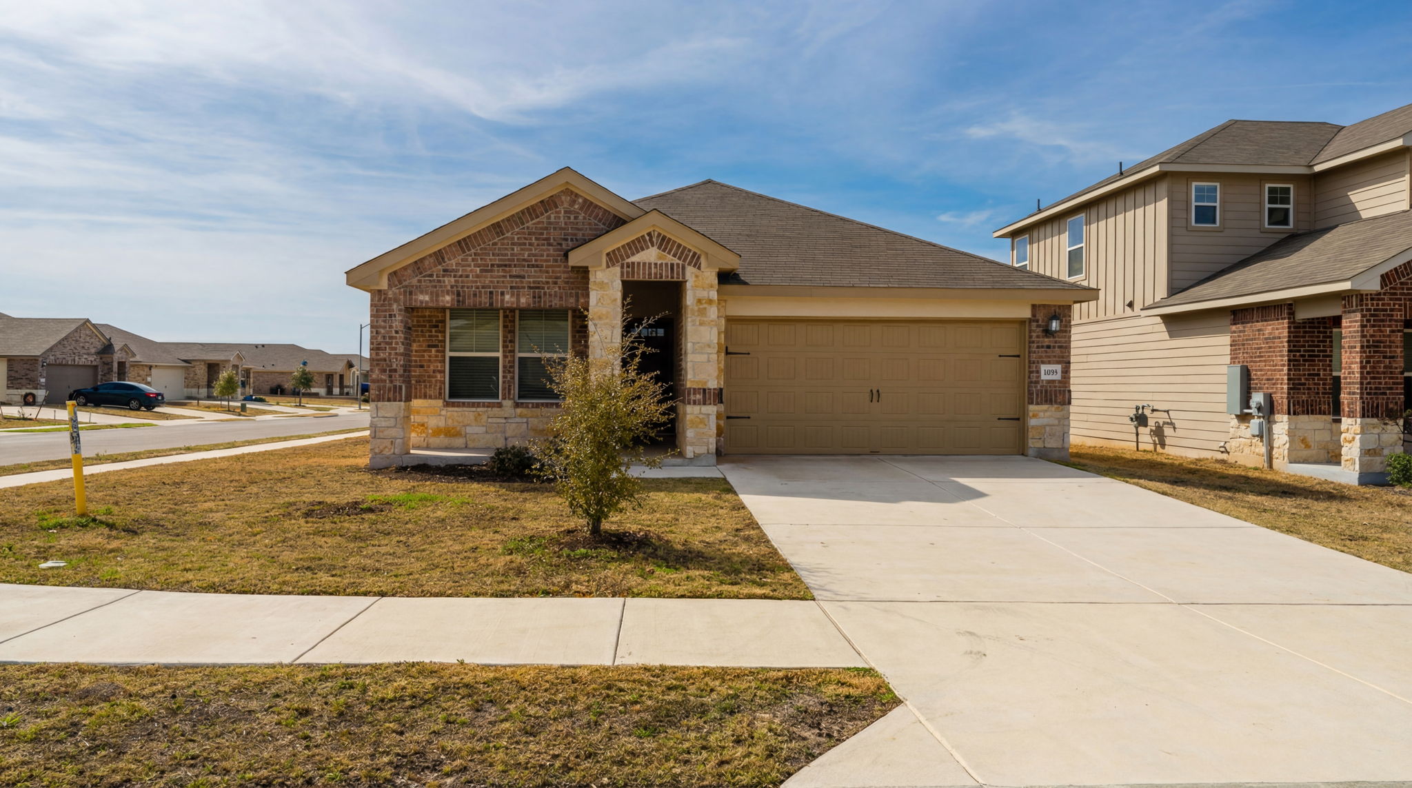 1003 Round Bale Road Hutto, TX 78634 - Photo 8 of 29 View of front of house featuring stone siding, concrete driveway, an attached garage, brick siding, and a front yard
