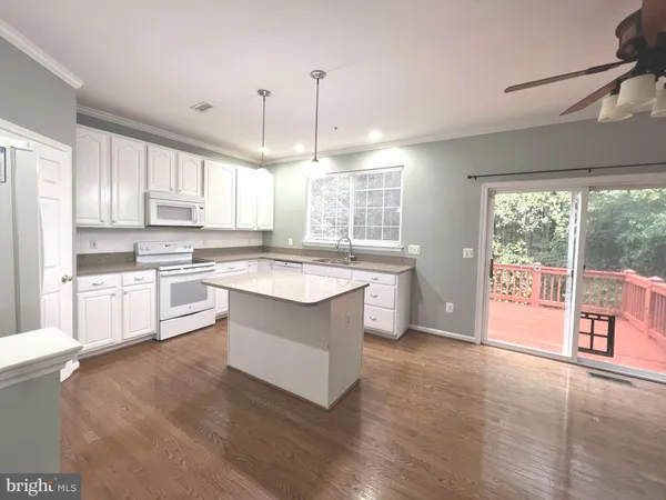 a large kitchen with kitchen island granite countertop a stove a sink a refrigerator and white cabinets with wooden floor