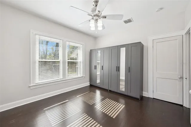 a view of an empty room with window a ceiling fan and wooden floor