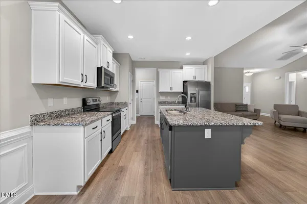 a kitchen with stainless steel appliances granite countertop white cabinets a sink a stove a microwave and cabinetry