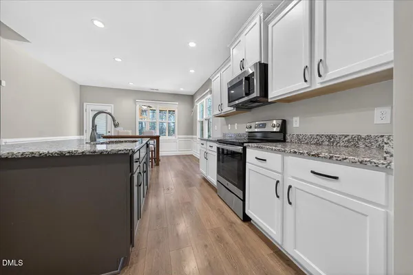 a kitchen with stainless steel appliances granite countertop wooden cabinets a sink a stove a dining table and chairs