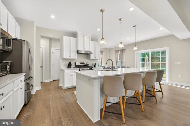 a kitchen with stainless steel appliances granite countertop a stove a white refrigerator a sink a dining table and chairs with wooden floor