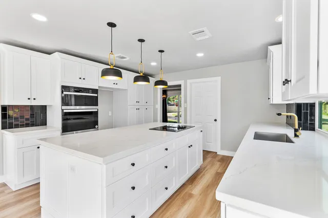a large white kitchen with a stove a sink a kitchen island with wooden cabinets and floors