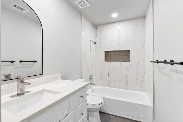 a bathroom with a bathtub shower sink vanity mirror and toilet