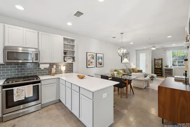 a open kitchen with stainless steel appliances kitchen island granite countertop a stove top oven a sink dishwasher and white cabinets