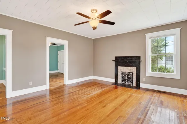 an empty room with windows a fireplace a ceiling fan and wooden floor
