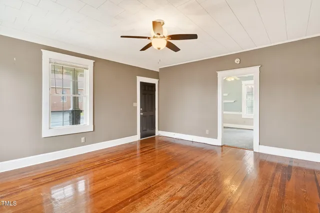 an empty room with wooden floor chandelier fan and windows