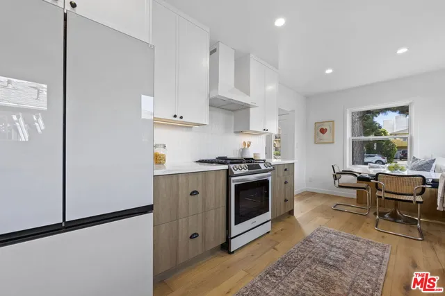 a kitchen with stainless steel appliances granite countertop a stove a sink a refrigerator and white cabinets with wooden floor