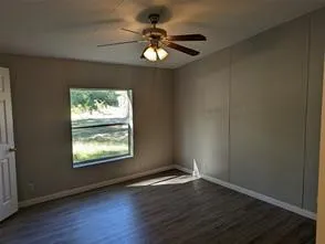 an empty room with wooden floor chandelier fan and windows