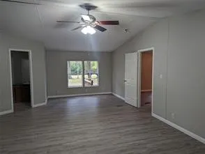 an empty room with wooden floor chandelier fan and windows