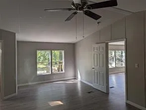 an empty room with wooden floor fan and windows