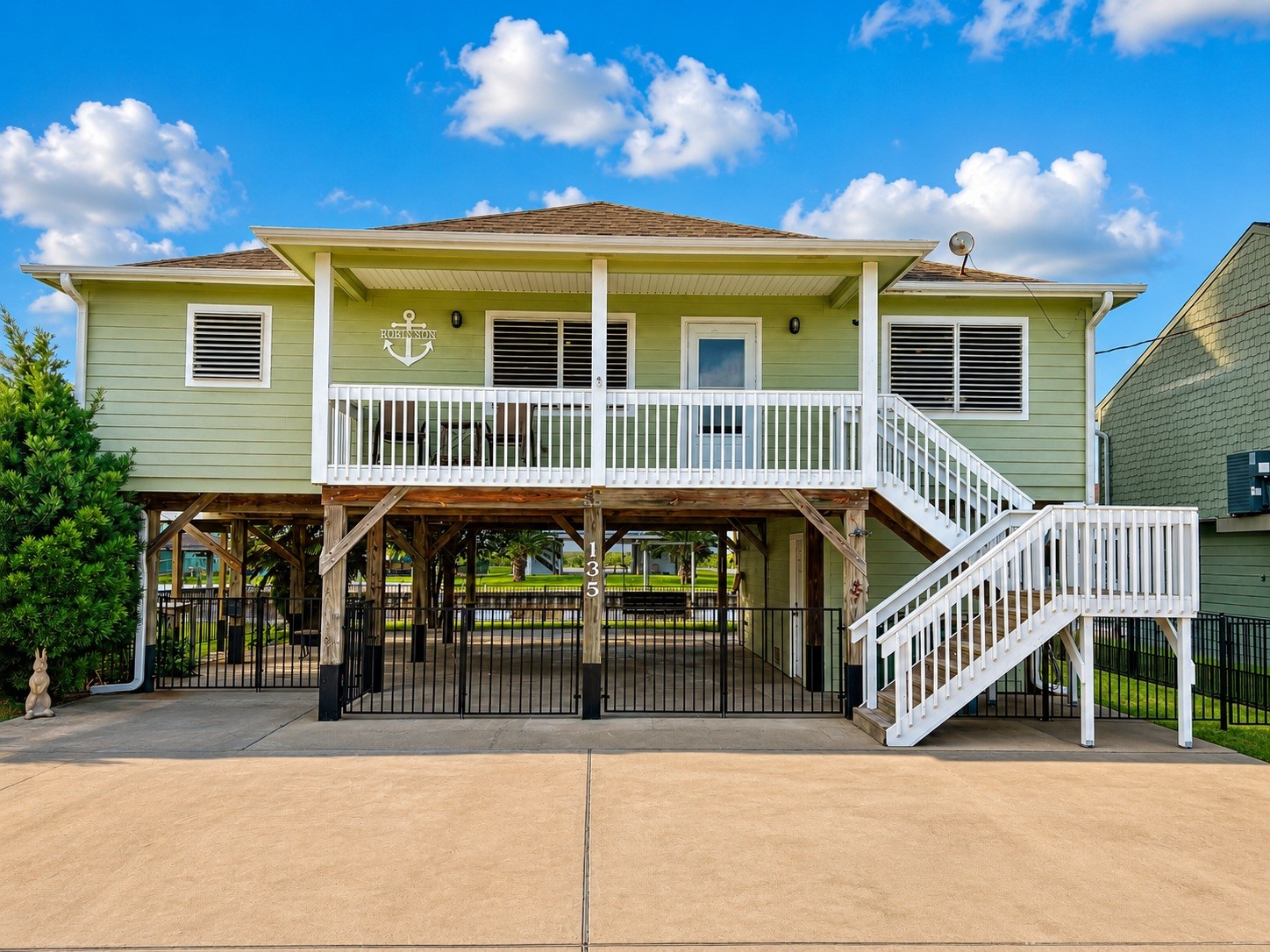 135 Sand Shoals Road Freeport, TX 77541 - Photo 1 of 20 This elevated home features a charming green exterior with white accents and a spacious front porch. The property includes a large concrete driveway and covered parking area underneath, offering a practical design for coastal living.