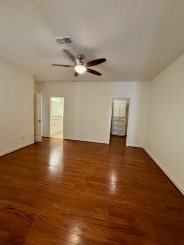 a view of an empty room with wooden floor and a ceiling fan