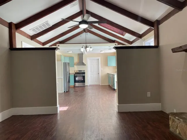 a view of a livingroom with wooden floor a ceiling fan and kitchen