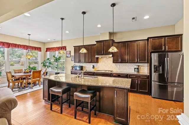 a kitchen with stainless steel appliances granite countertop a stove refrigerator sink dining table and chairs