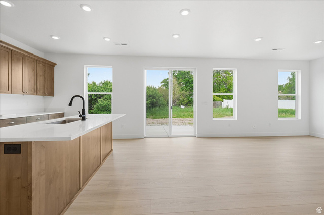 844 North 400 West Logan, UT 84321 - Photo 8 of 43 Open-concept living space with light wood-finish flooring, a kitchen island featuring a sink and matte black faucet, recessed lighting, and multiple windows providing natural illumination