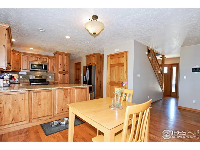 a kitchen with stainless steel appliances kitchen island granite countertop a refrigerator a stove top oven and a dining table with wooden floor