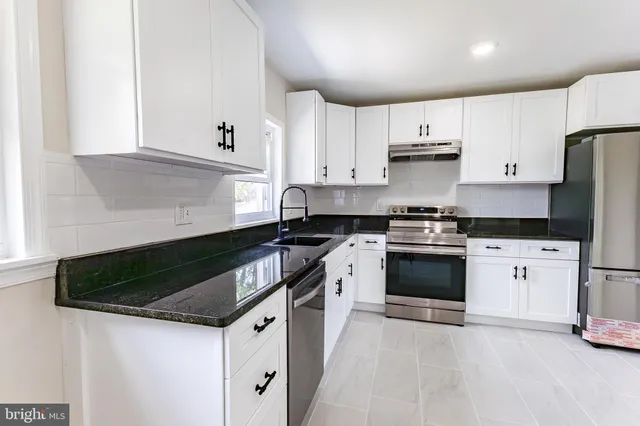 a kitchen with stainless steel appliances granite countertop a stove a sink and white cabinets