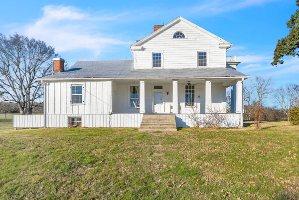 a view of white house with a big yard and large trees