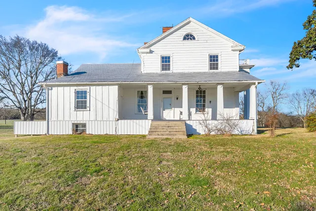 a view of white house with a big yard and large trees